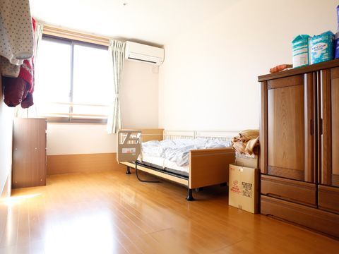 入居者の部屋にはエアコンが取り付けられており、窓からは外の光が差し込んでいる。介護ベットやタンスもある。