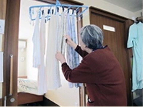 鴨居にかけられたピンチハンガーに洗濯物を干している女性入居者様