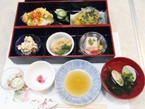薄い色で絵が描かれている紙の上に置かれた、松花堂弁当風のお食事