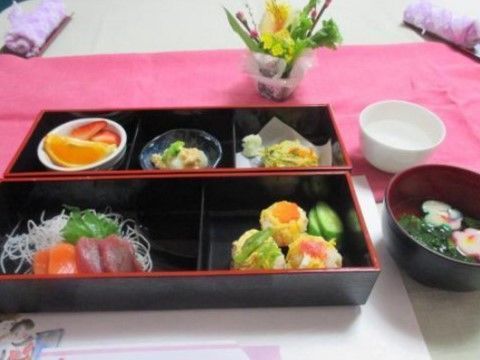 白色の紙とピンク色の布にまたがって置かれている、松花堂弁当風のお食事