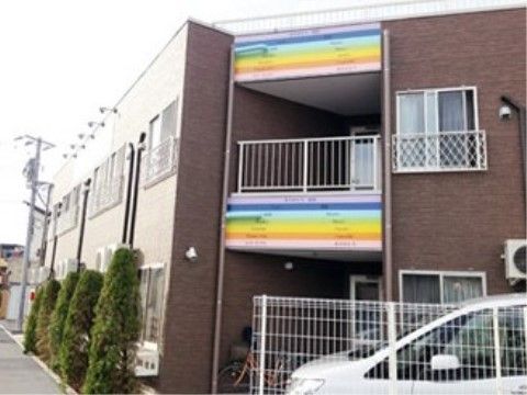 壁の一部がカラフルに塗られ、白いフェンスの向こうに車が停まっている施設外観