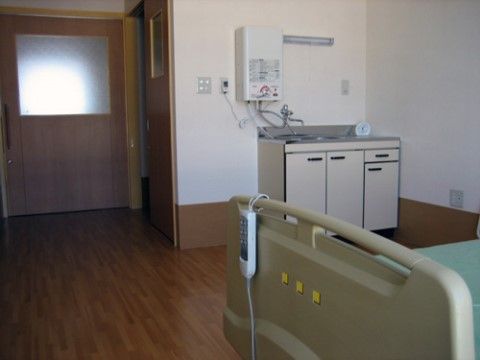 室内には介護用ベッド、簡易キッチンが設けられている。居室の床はフローリングになっており、入り口には引き戸が設置されている。