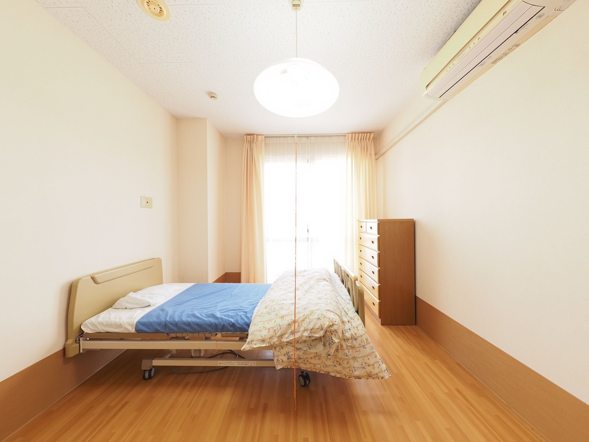 居室にはカーテンのついた窓がある。タンス、エアコン、ベッドが完備されており、床はフローリングになっている。