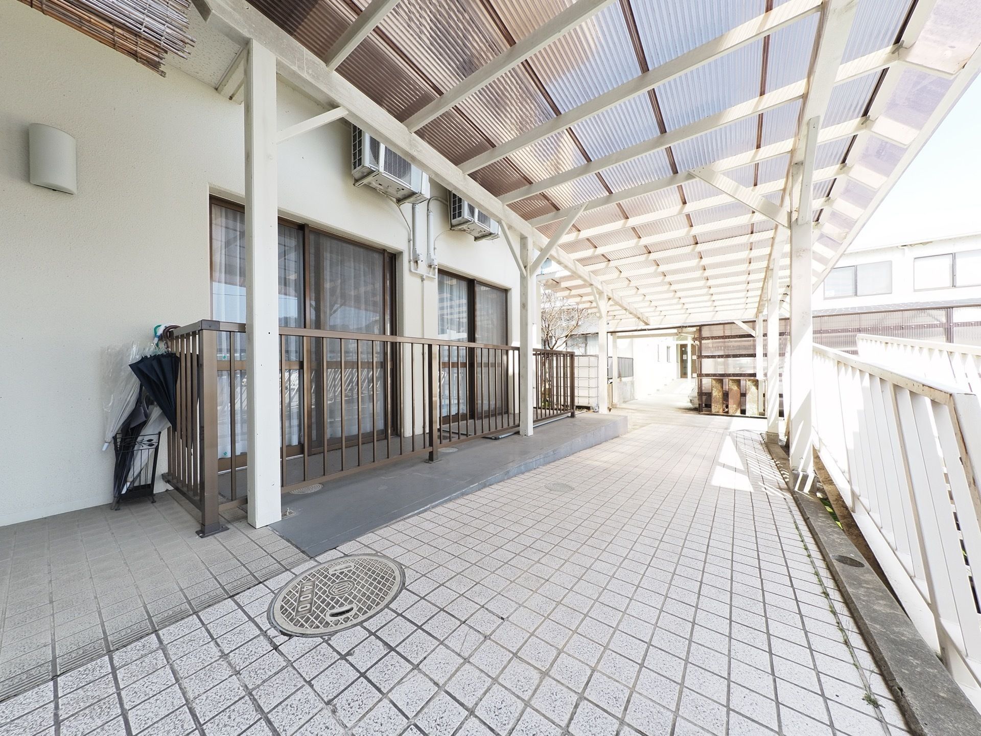 施設の外に設けられた廊下には屋根がついており、地面には白いタイルが貼られている。またそこに隣接した居室のバルコニーには柵がある。