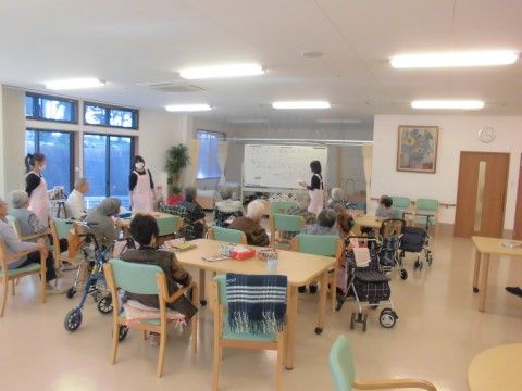 ピンク色のエプロンをした女性スタッフの話を聞いている入居者様たち