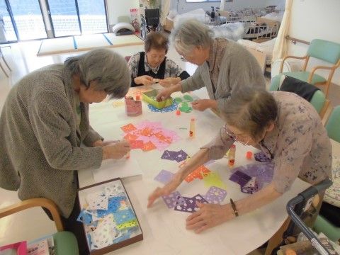 テーブルに集まって、いろいろな色の紙を使って創作をしている女性入居者様たち