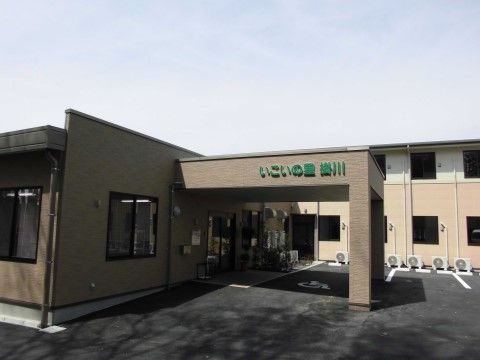 建物の壁は白色系およびベージュ系の配色になっている。玄関には屋根が設けられ、スロープがつながっている。