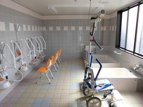 浴室はタイル張りで大きな窓があり、浴槽には手すりが設置されている。機械浴のための介護用チェアも置かれている。