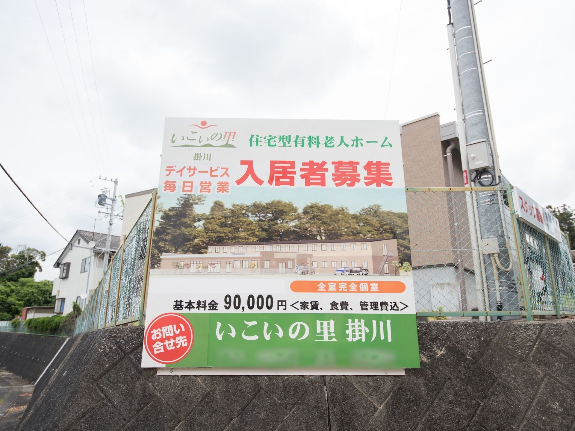 ブロックとネットで囲まれた敷地の曲がり角に、看板が設置されている。施設名称だけではなく、建物の外観や基本料金、問い合わせ先が明記してある。