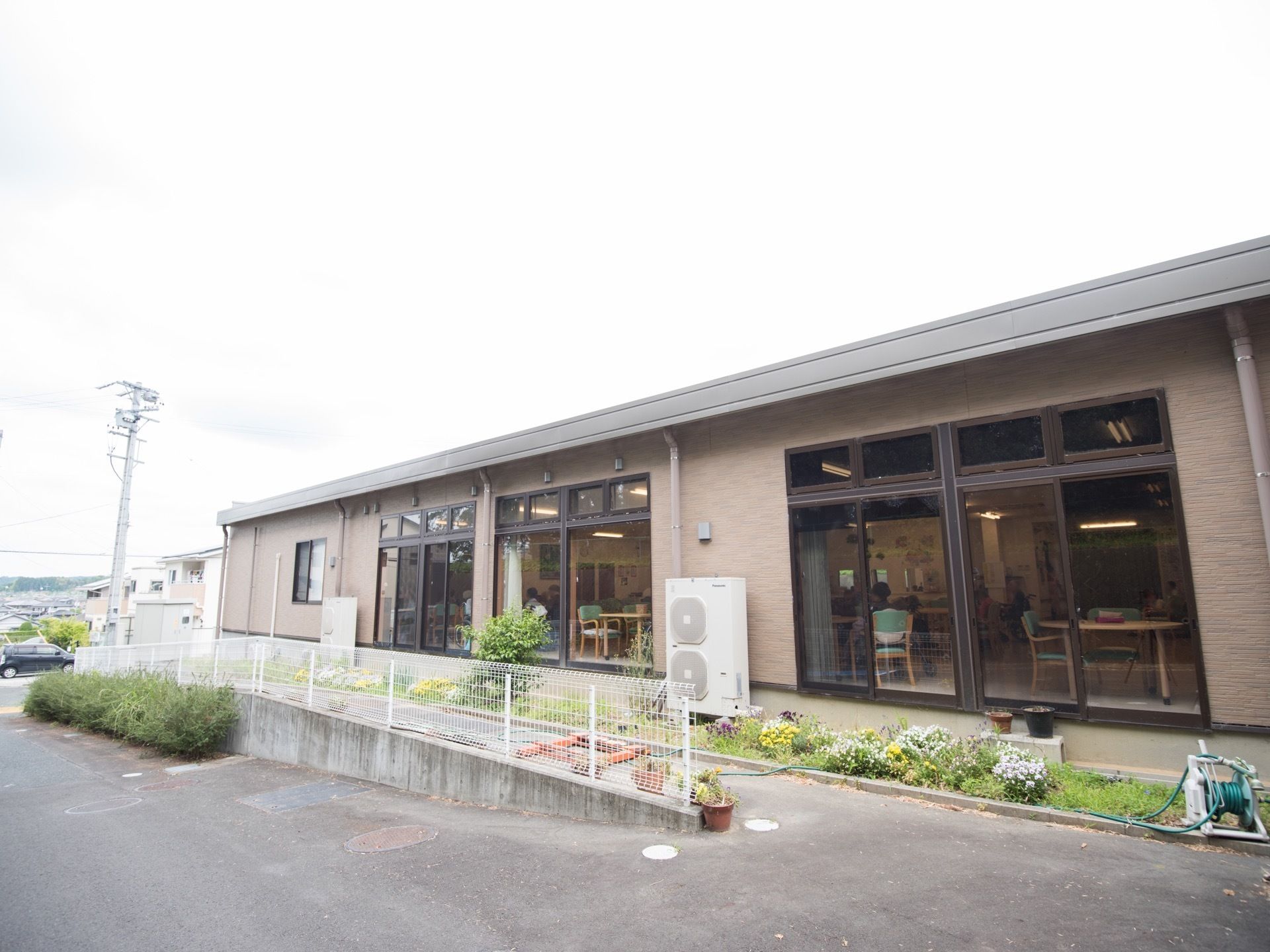 掃き出しの窓が並ぶ茶色い建物の前面に、花壇がある。建物の周囲はアスファルトで舗装されており、左側は車道に向かって緩やかな傾斜になっている。