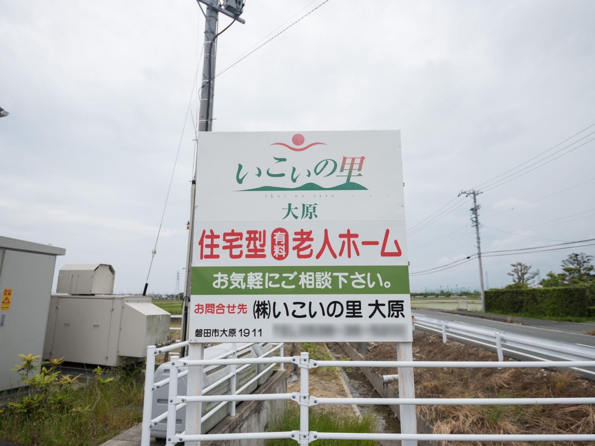 緑豊かな畑が広がっている道路の脇に、施設紹介の看板が立てられている。住所や問い合わせ先が書かれ、気軽に相談できるようになっている。