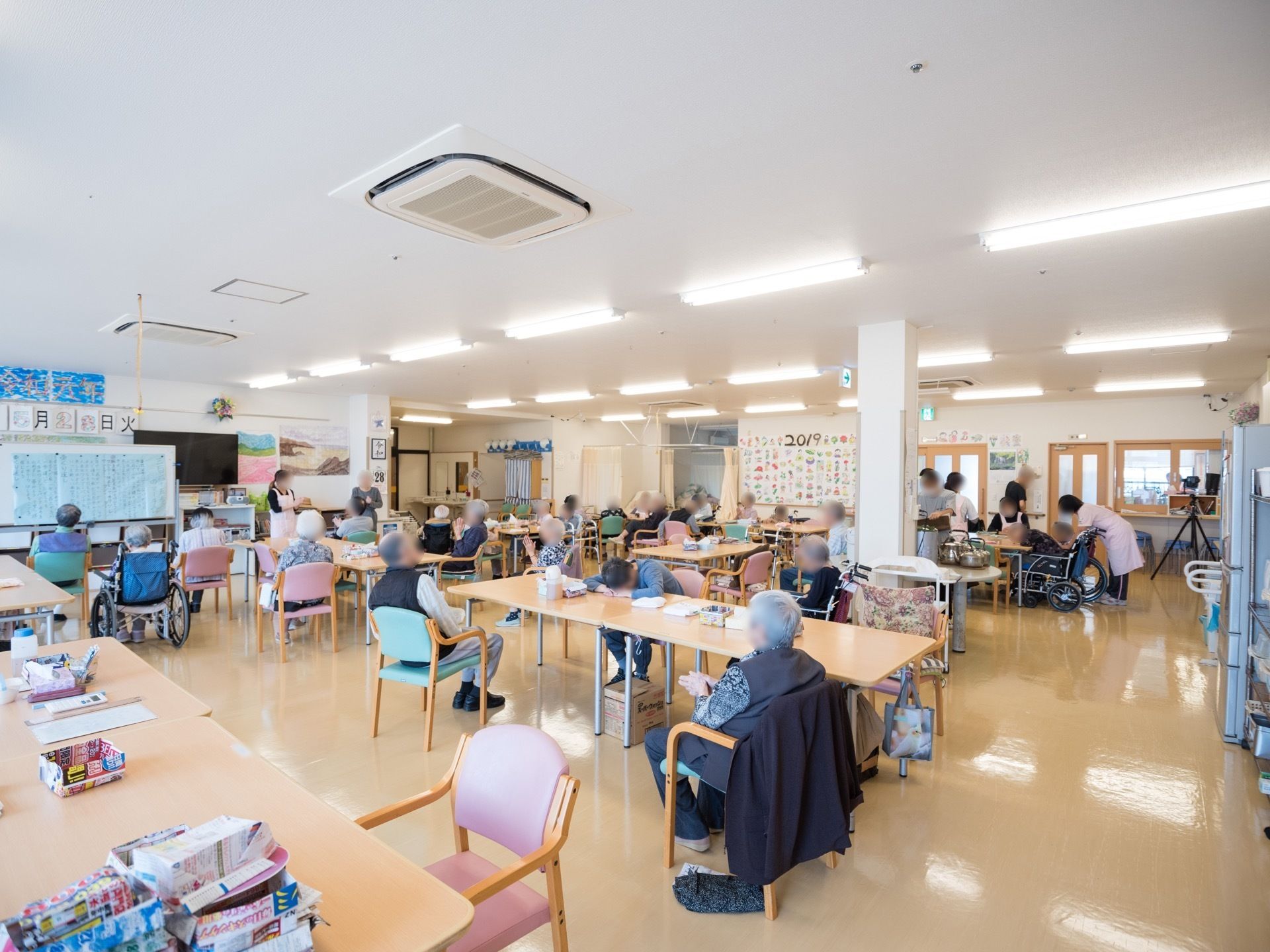 明るく広い室内にはテーブルが縦に並べられ、入居者様が前方を見やすいように配置されている。室内には手作りの装飾が施され、親しみやすい雰囲気。