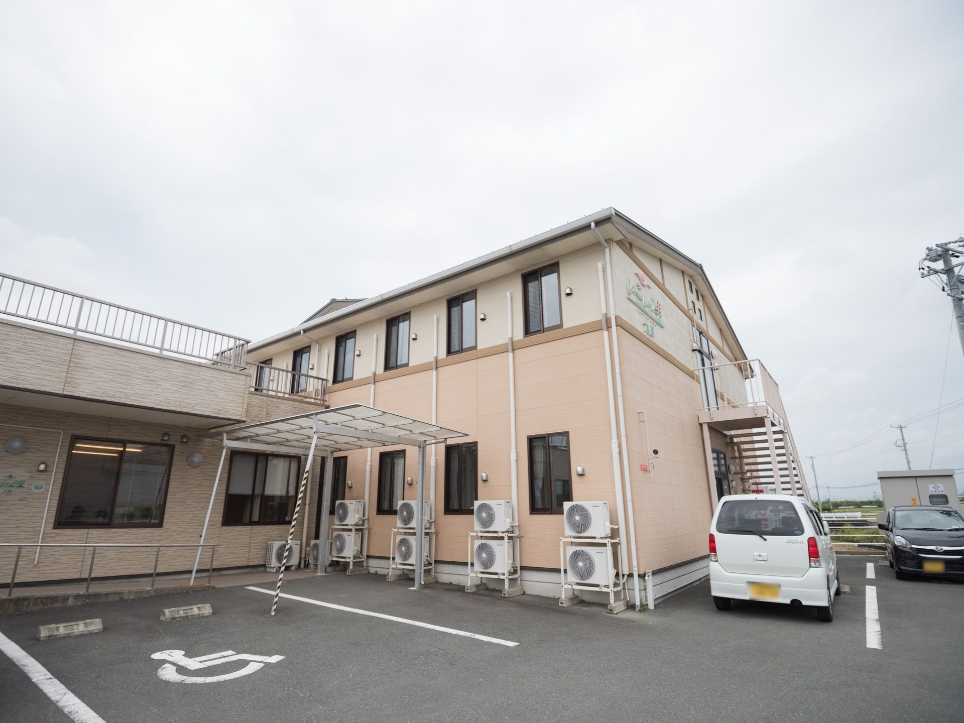 2階建ての明るい外装の建物と、平屋建てのモダンな建物とがくっついて１つの施設を形成している。裏手には駐車スペースも完備されている。