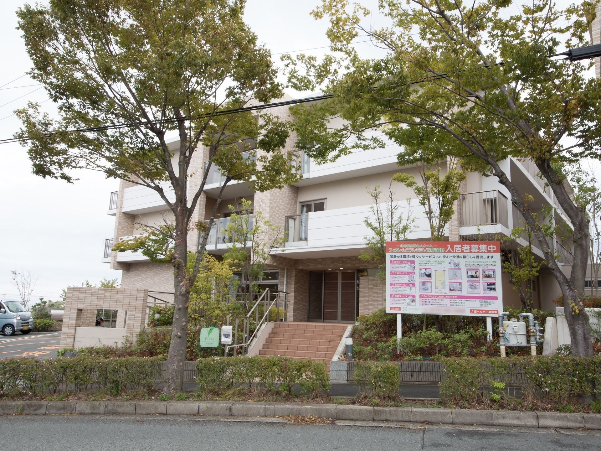 木々に囲まれた、落ち着いた雰囲気の３階建ての建物。玄関まで階段になっているが、しっかりとした手すりが取りつけられている。