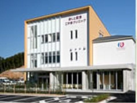 一部の外壁がオレンジ色の建物である。縦長の窓が付いている。クリニックの前は駐車スペースが設けられている。
