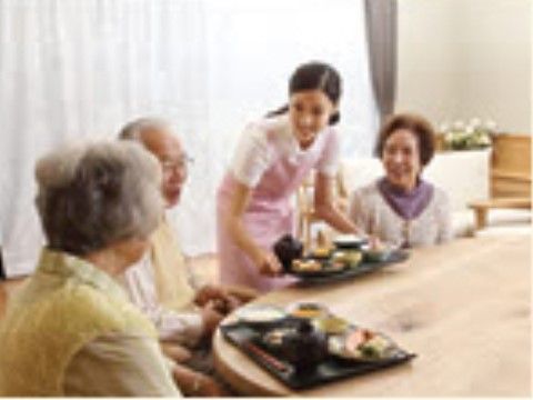 椅子に座って、女性スタッフが運ぶお食事を待っている入居者様たち