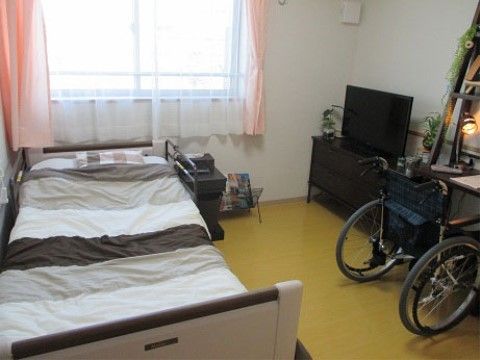 居室にあるベッドには、枕を置く方に柵がついている。ピンク色のカーテンがある窓からは、日の光が入ってくる。
