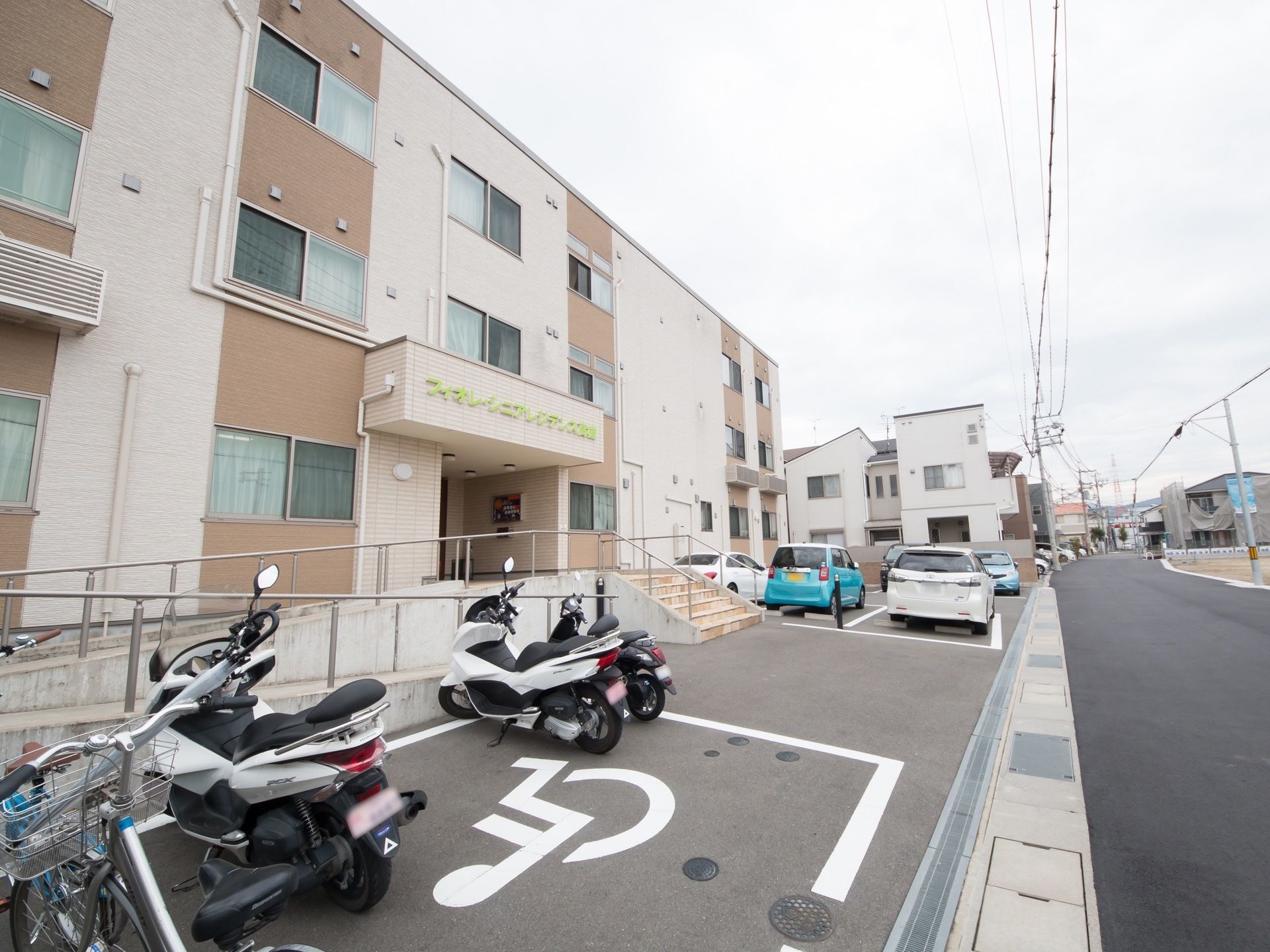 落ち着いたベージュ色の３階建ての建物がある。道路に面した部分が駐車場となっており、車の出し入れがしやすいようになっている。