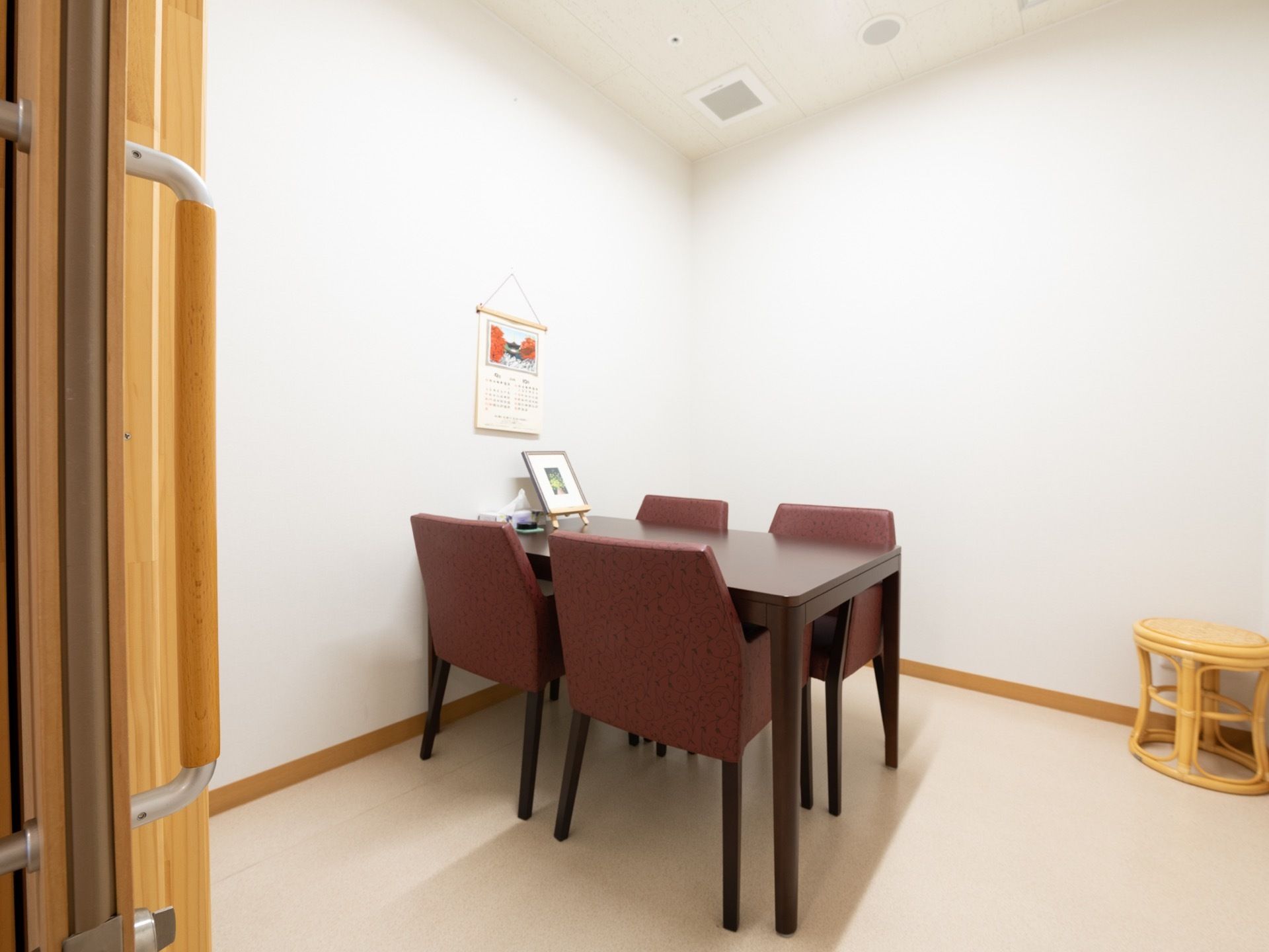 白い壁のシンプルな部屋に、4人掛けのテーブルセットが置かれている。壁にはカレンダーが掛けられている。