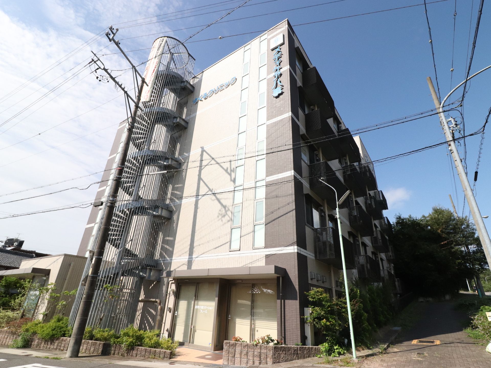 施設の前は歩道があり、街路樹なども植えてある。居室のスペースには、ベランダがある。らせんの外階段がついている。