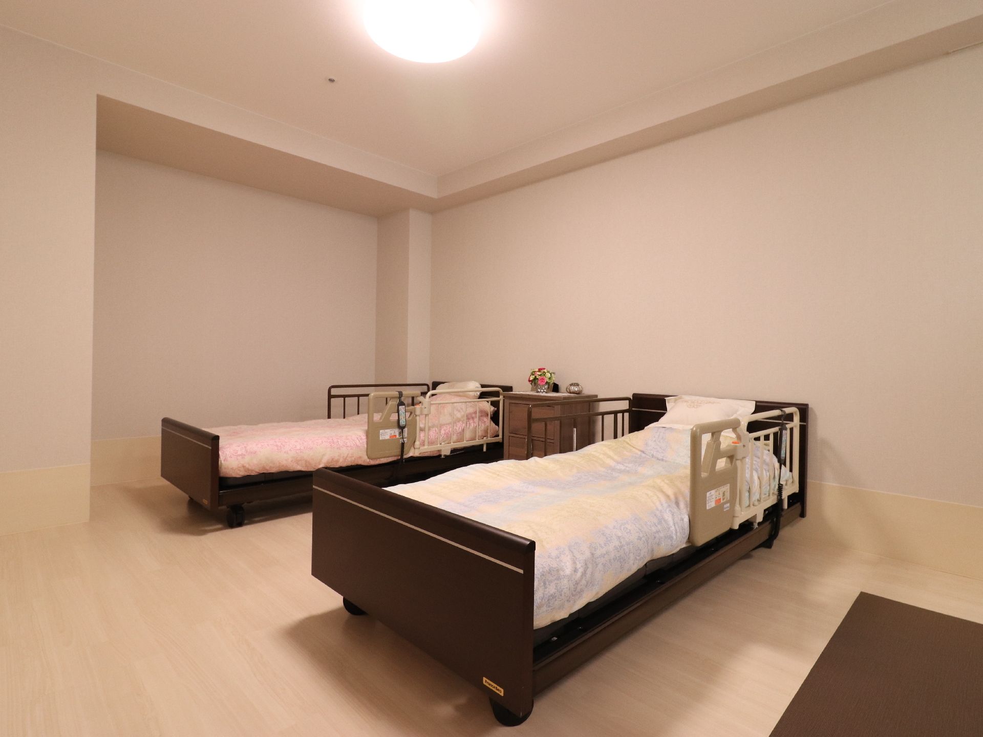 2人部屋には介護用ベッドも2台完備される。白の壁にダークブラウンのベッドがマッチしている。両側に柵があるので安心である。