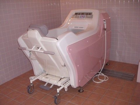 ピンク色の外枠がついた、可動式の椅子と一体型の介護入浴設備