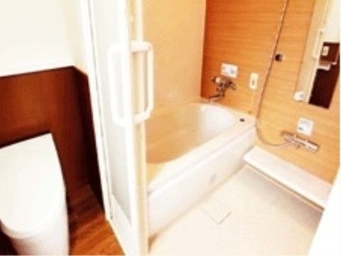 トイレの床は木目調のフローリングになっており、後ろの壁は下半分が茶色で、上半分は白くなっている。隣の浴室には鏡が取り付けられている。