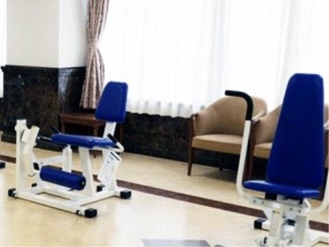 機能訓練のための器具が設置されている。後ろにはソファーがあり、休憩ができる。大きな窓にはレースのカーテンが付けられている。