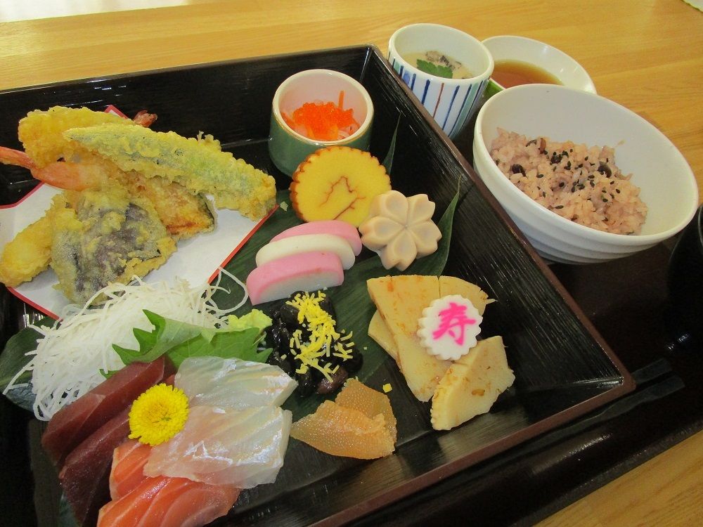 刺身や天ぷらの盛り合わせと黒豆や数の子が入ったおせち料理と赤飯のセット