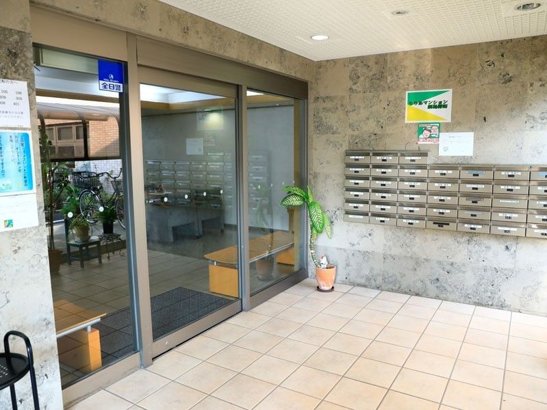 入口は自動ドアである。ドアの外側には入居者様の郵便受けが並んでいて、その近くには観葉植物が置かれている。