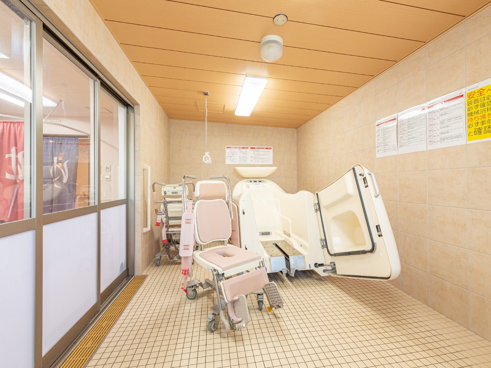 ピンク色の座面や背もたれがついた可動式の椅子が置かれている介護浴室