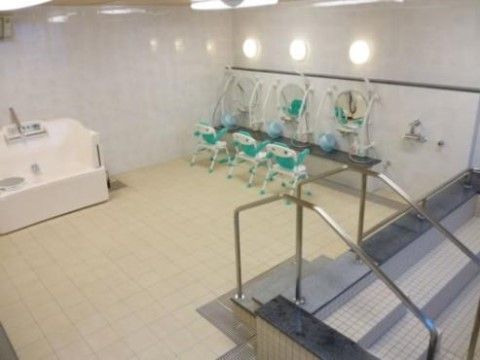 手すりが付いた広い浴槽のほかに、３人分のシャワーとチェアが置かれており、介護用の浴槽も設置されている。