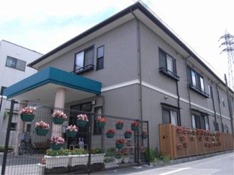 敷地境界のフェンスに、たくさん花が咲いているプランターがかけられている施設外観