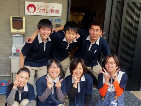 玄関前でピースサインをしたり肩を組んだりして、集合写真に収まっているスタッフ