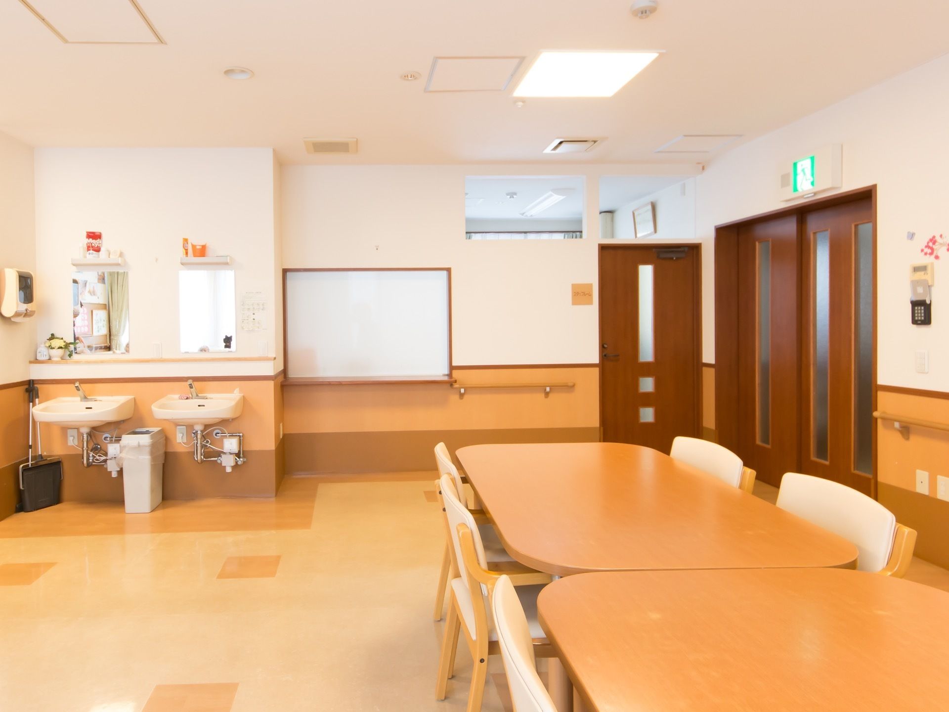 明るく広々とした共有スペースには、大きなテーブルセットが並べられている。部屋の角には鏡付きの洗面台が２台備わっている。