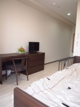 ベージュで統一された室内。木目調の家具を配置し落ち着いた雰囲気になっている。ベッドには落下防止用の柵がある。