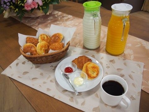 パンが入ったバスケットや、牛乳とジュースのボトルが置かれている朝の食卓