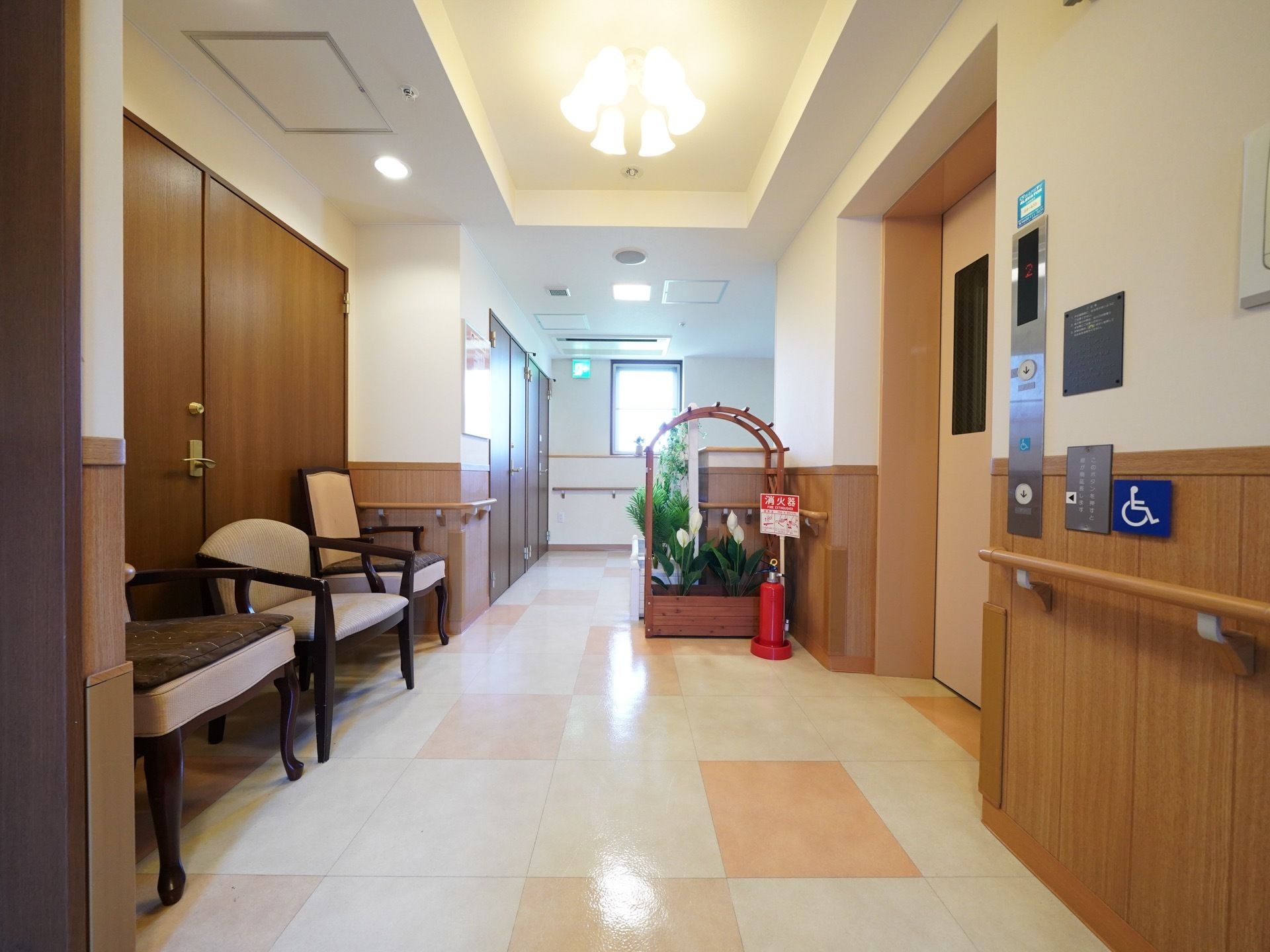 綺麗なタイルが床に使用されている。壁には手すりが取り付けられている。エレベーター前には椅子が置かれている。