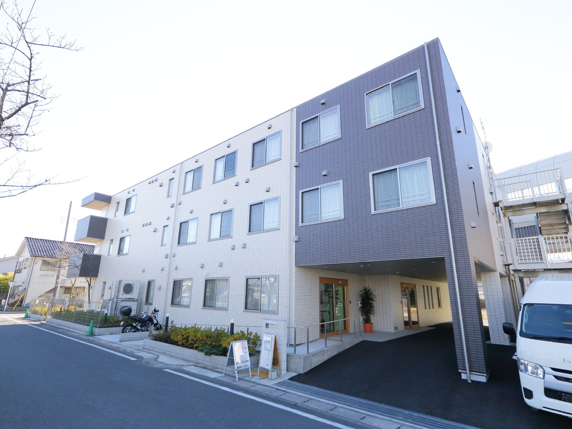 3階建てのサービス付高齢者向け住宅。玄関前に駐車スペースが設けられている。周りには大型ショッピングセンターがあり、利便性に優れている。