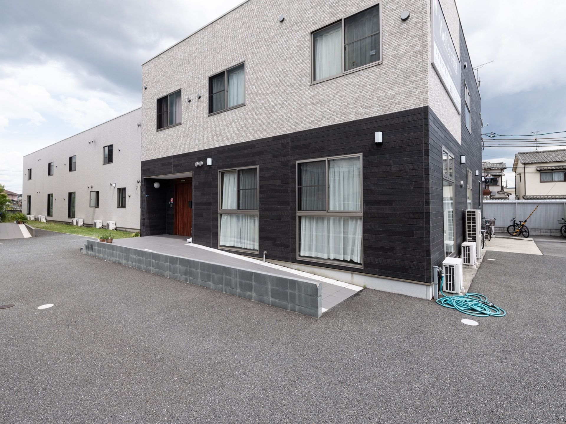 大きな一軒家のような外観の２階建ての建物で、入口前には緩やかな傾斜のスロープがある。建物前には駐車できるスペースがある。