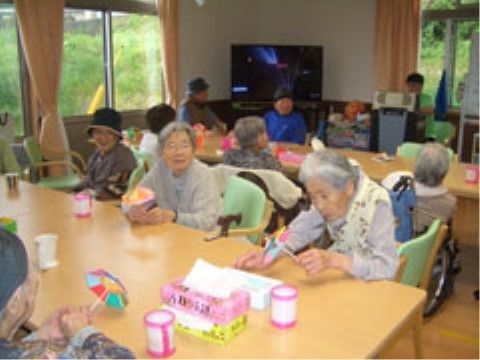 テーブルに集まって、色紙と竹ひごで作った創作物を手に持っている入居者様たち