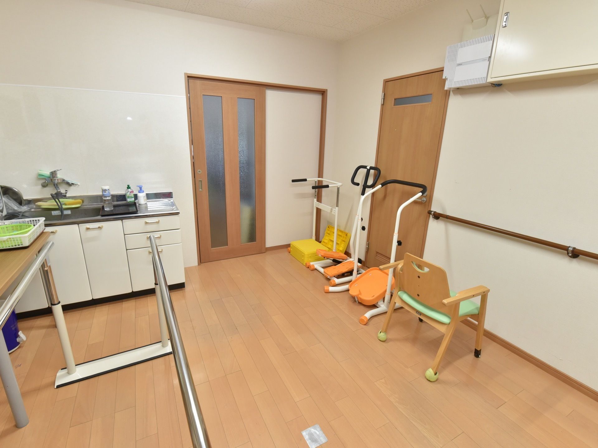 フラットな床の共有スペースには、体力を維持するための器械や手すり台が置かれている。奥にはキッチンスペースがある。