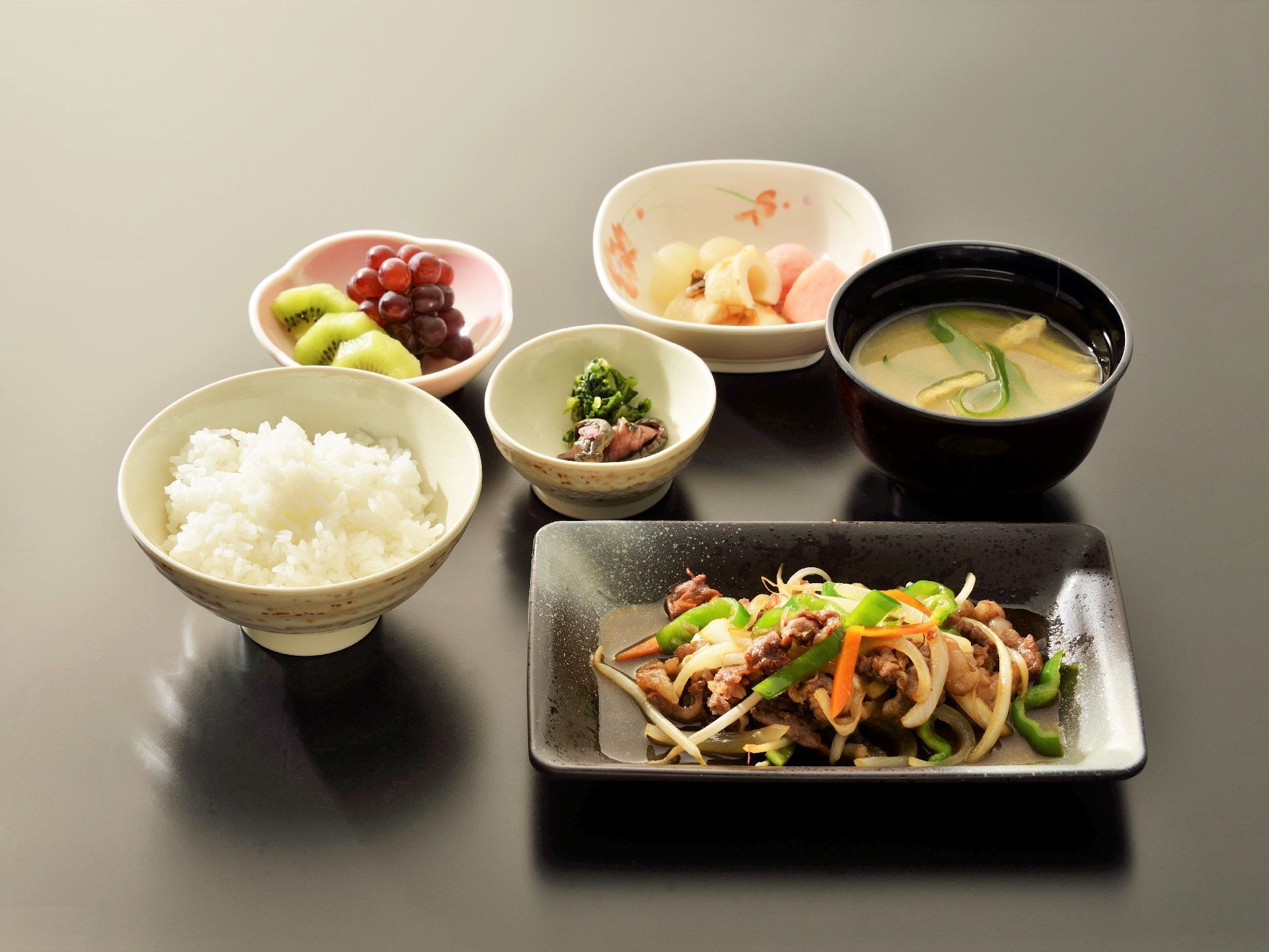 テーブルの上に料理が6品載っている。ご飯、みそ汁、和え物、果物、おでん、野菜炒めが載っている