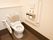 温水洗浄便座機能付きのトイレが設置されている。便器の周囲には手すりと背もたれが取りつけられており、壁には緊急通報装置がある。