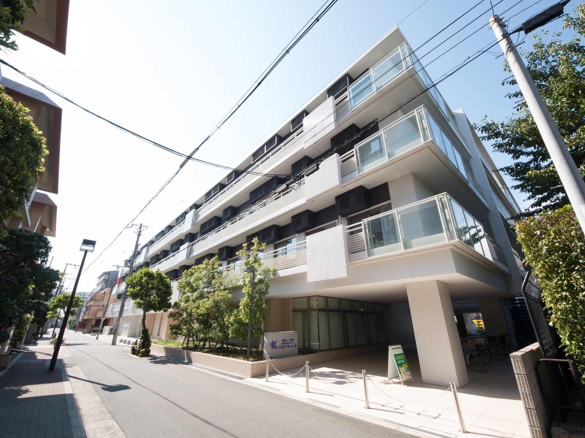 建物の入口は広い玄関ポーチがあり、道路との境には車止めが設置されている。周囲には木が多く植えられている。