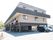 ３階建ての建物で濃いブラウンと淡いブラウンを組み合わせたモダンな外観デザインとなっている。建物の横には駐車場がある。