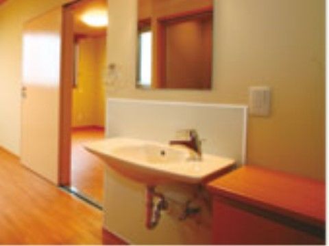 暖色系の照明と木目調のフローリングを採用した、温かみのある居室である。足元に空間のある洗面台を完備している。