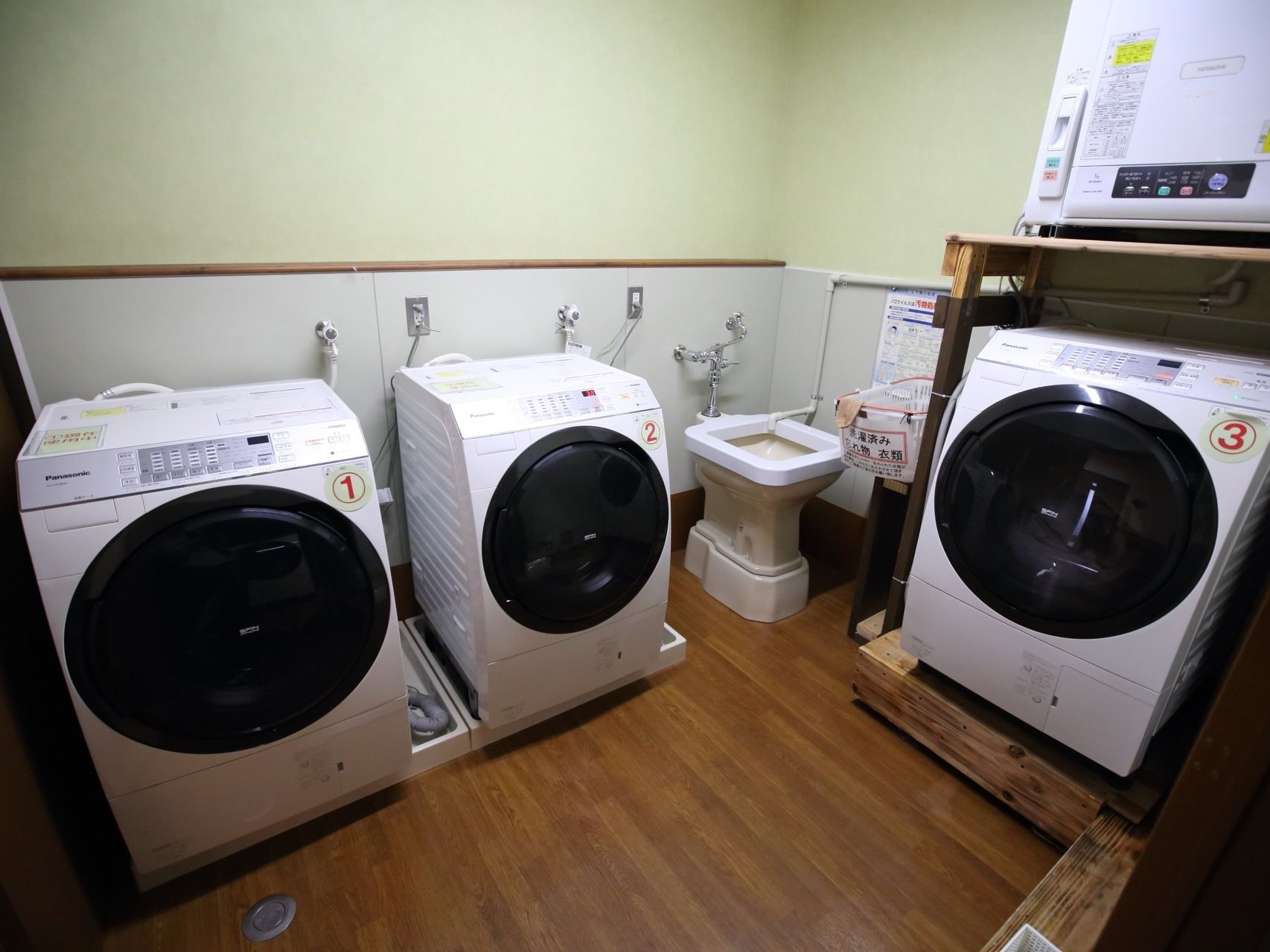 ３台の全自動洗濯機が設置され、１台の乾燥機と汚物処理専用の洗い場が設けられている施設内の洗濯室である。
