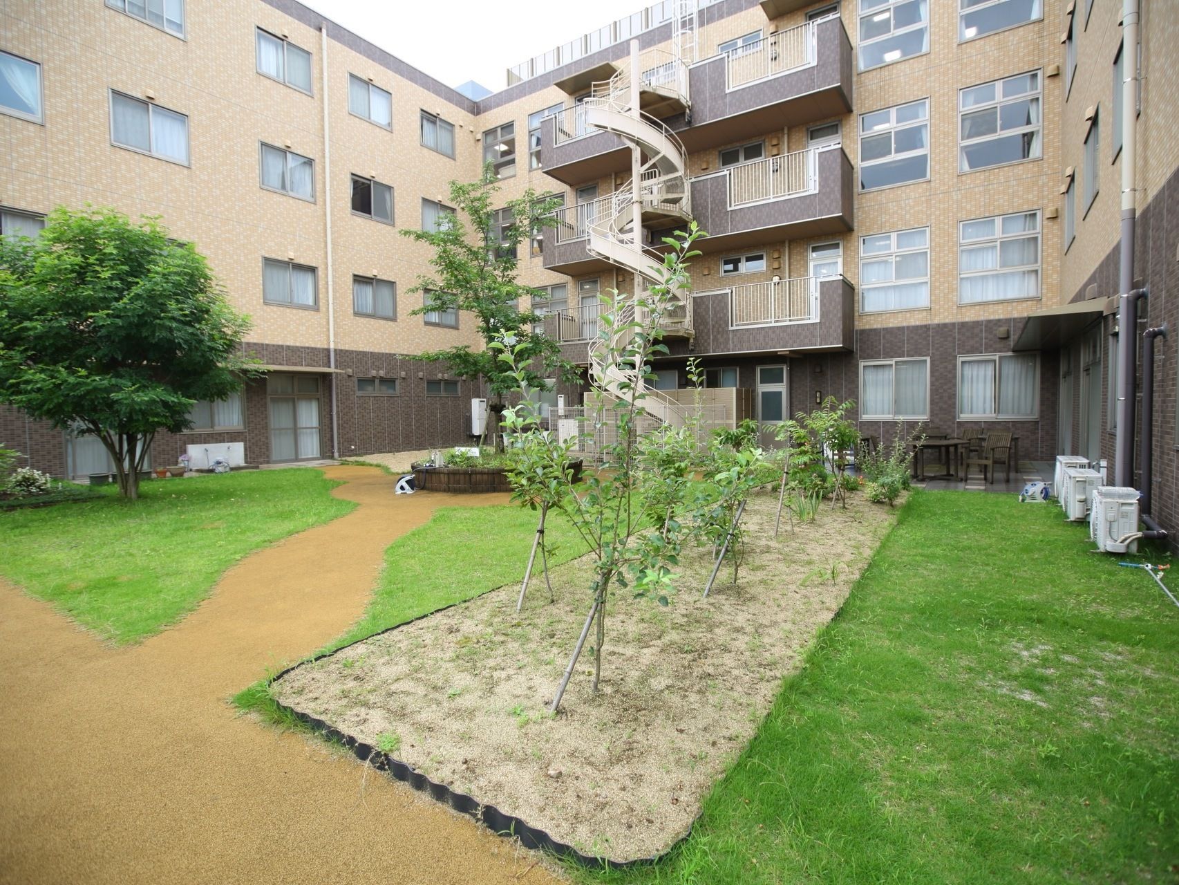 施設の中庭の様子である。緑を配した花壇や植え込みがあり、緊急時の屋外への脱出ルートの螺旋状のすべり台が完備されている。