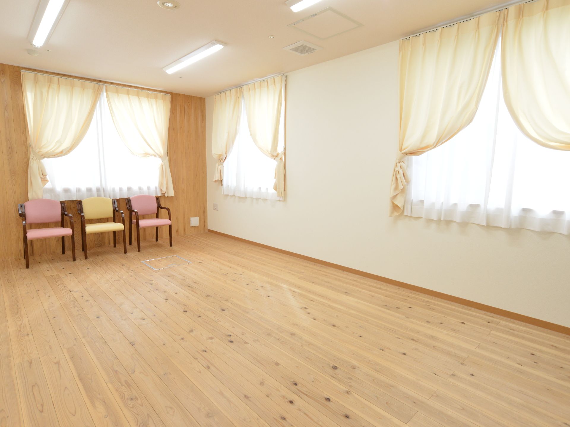 広々とした木目調の空間には、ひじ掛け付きのいすが3脚完備されている。カーテンがおしゃれに掛けられている。